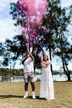 a man and woman are holding pink confetti in front of their faces as they stand under a tree