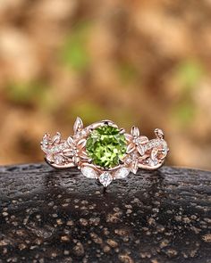 an engagement ring with a green stone surrounded by white diamonds on top of a rock