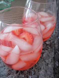 two glasses filled with ice and strawberries on top of a granite counter next to each other