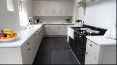 a kitchen with white cabinets and black flooring next to a bowl of fruit on the counter