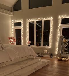 a bedroom with lights on the windows and a bed covered in white sheets, pillows and blankets