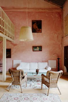 two wicker chairs and a table in a room with pink walls, white couches and paintings on the wall