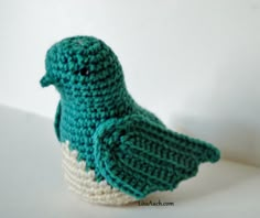 a crocheted green bird sitting on top of a white table next to a wall