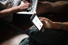 two people sitting on the floor with their laptops and one is holding an iphone