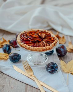 there is a pie on the table with fruit around it and gold utensils