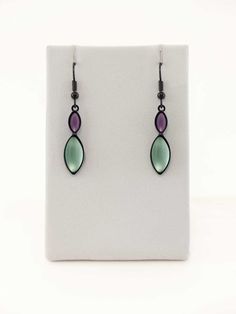 earrings with green and purple glass tears hanging from black cords on a white background