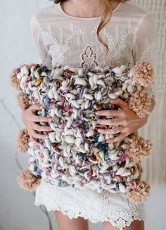 a woman is holding a pillow made out of knitted yarns and wool balls