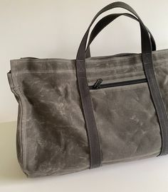 This extra-large 13.5 oz waxed canvas tote is rugged and spacious. My original design is unique and stylish. The rounded bottom provides extra space for bulky items.  There's a large interior zippered pocket and an exterior zippered pocket. 10.10 oz Army Duck Canvas is treated with 3.5 oz of wax and is heavier than most waxed canvas bag fabrics.  Army Duck is tightly woven and very strong.   The bag is 18" wide x 10" deep, sides are 13" high. Zippered pocket inside measures 16" x 7". Outside poc Practical Cotton Bags With Waxed Finish, Practical Duck Canvas Bag For Everyday Use, Duck Canvas Weekender Tote Bag For Everyday Use, Waxed Canvas Bag For Daily Use, Practical Everyday Waxed Canvas Bag, Everyday Canvas Weekender Bag With Zipper Closure, Everyday Canvas Weekender Bag With Zipper, Casual Waxed Finish Weekender Bag, Casual Waxed Weekender Bag For Everyday