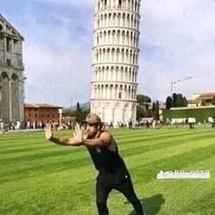 a man is standing in front of the leaning tower with his hands out to catch something