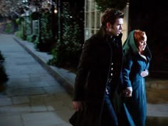 the man and woman are walking down the street at night, one is holding her hand