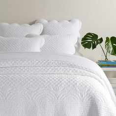 a bed with white sheets and pillows next to a potted plant on a nightstand