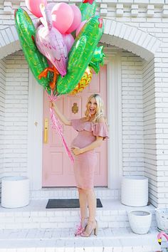 a pregnant woman holding balloons in front of a pink door