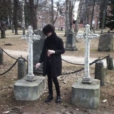 a woman in black coat standing next to two crosses with chains on the ground behind her