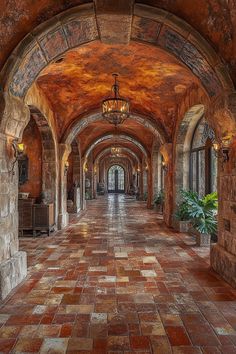 an arched hallway with brick flooring and stone arches on both sides is lit by a chandelier that hangs from the ceiling