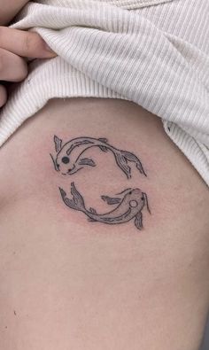 a woman with a tattoo on her stomach that has two fish swimming in the circle