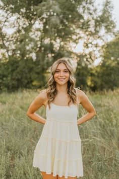 a woman standing in tall grass with her hands on her hips and smiling at the camera