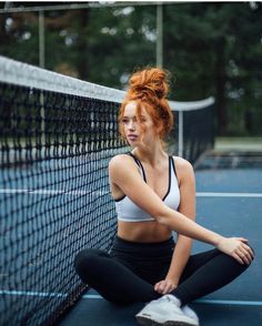 a woman with red hair sitting on a tennis court