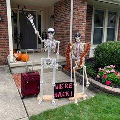 two skeleton statues in front of a house with we're back written on the sign