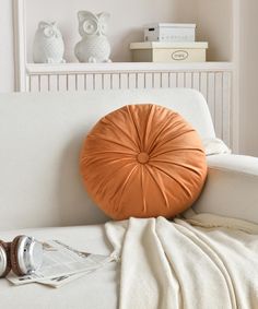 an orange round pillow sitting on top of a white couch next to a stack of books