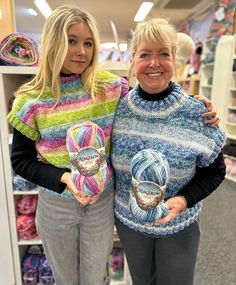 two women standing next to each other holding knitted items