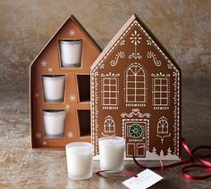 a gingerbread house shaped candle holder with three candles in front of it and a red ribbon on the side