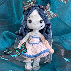 a crocheted doll with blue hair wearing a dress and butterflies on her head