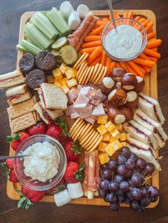 a platter filled with cheese, crackers, fruit and veggies next to dip