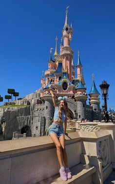 a woman standing on some steps in front of a castle with her arms raised up