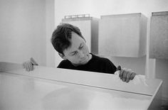 black and white photograph of a man wiping his face in front of a washer