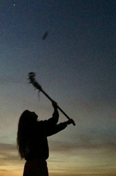 a woman holding a broom in the air at sunset or dawn with her arms outstretched