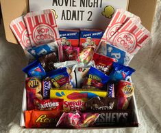 a box filled with candy and snacks on top of a white sheet covered bed next to a movie night sign