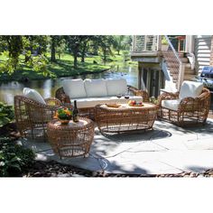 wicker patio furniture set with white cushions in front of a lake and house on the other side