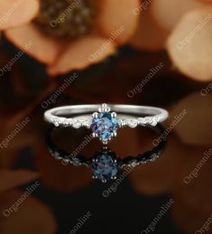 an engagement ring with blue and white diamonds on the side, sitting in front of flowers