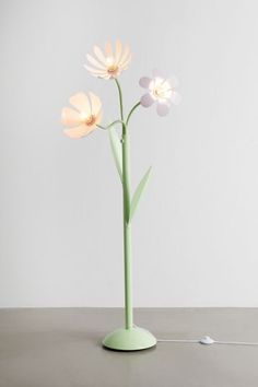 a green vase with three white flowers in it on a table next to an electrical cord