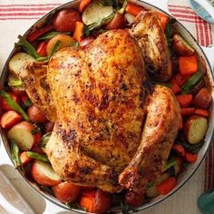 a roasted chicken and vegetables in a pan on a tablecloth with utensils