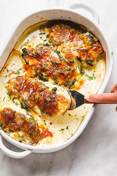 a hand holding a spoon over a casserole dish with chicken and spinach