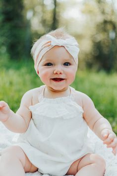 a baby sitting in the grass wearing a white dress