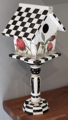 a birdhouse with roses painted on it sitting on top of a wooden table next to a wall