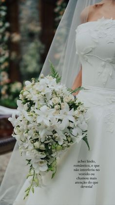 a woman in a wedding dress holding a bridal bouquet with white flowers on it