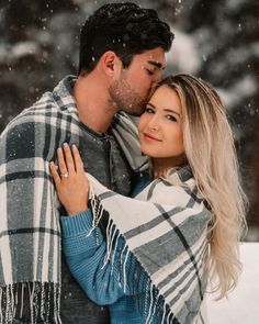 a man and woman wrapped up in blankets smile at each other as they stand in the snow