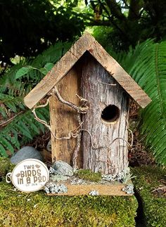 a wooden birdhouse sitting on top of a moss covered ground next to a sign