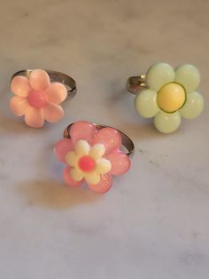 Simple flower rings! Your choice of style, all made with stainless steel adjustable bands.  Available in: Pale pink with pastel pink center (Top left of 1st photo) Pastel pink with white and hot pink center (Bottom middle of 1st photo) Mint with buttery yellow center (Top right of 1st photo) Glued down with gorilla glue and tested ensure the plastic cabochons don't come off. I would still try to avoiding pulling on the flowers with great force as this may loosen/remove the cabochon. I found that Spring Pink Flower Ring Gift, Adjustable Pink Flower Shaped Rings, Pink Ring For Spring Gift, Cute Handmade Pink Rings, Pink Ring As Spring Season Gift, Spring Gift Pink Ring, Spring Gift Pink Rings, Pink Rings Suitable For Spring Gift, Cute Pink Round Rings