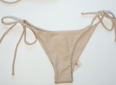 Get ready to hit the beach in style with our Isla Bikini Bottom! Featuring a chic beige color and side-tie design, this bikini bottom will flatter your figure and add a touch of elegance to your swimwear collection. Perfect for a day of fun in the sun, make a statement with our Isla Bikini Bottom! Our versatile collection is eco-friendly! It is produced with the Amni® Soul Eco, the world’s first biodegradable yarn, has an enhanced polyamide 6.6 formula allowing clothes to quickly decompose after being properly discarded. This technology keeps the durability and quality of the garments while still offering the polyamide fiber benefits (soft touch, comfort, easy care, etc.) Degrading in around three years*, the Amni® Soul Eco solution decomposes ten times faster than conventional polyamides Chic Beige Stretch Swimwear, Stretch Cream Bottoms For Beach, Stretch Cream Bottoms For The Beach, Summer Beach Bottoms In Neutral Color, Cream Stretch Bottoms For Beach, Neutral Summer Bottoms For Beach, Cream Stretch Bottoms For The Beach, Neutral Summer Beach Bottoms, Chic Beige Swimwear For Poolside