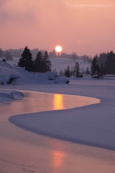 the sun is setting over a frozen lake