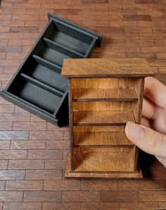 a hand is holding a small wooden box with drawers on the floor next to it