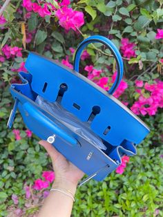 a hand holding a blue purse in front of pink flowers