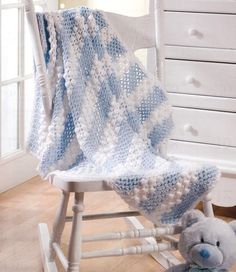 a crocheted baby blanket sitting on top of a rocking chair next to a teddy bear