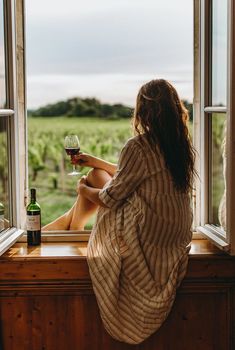 a woman sitting on a window sill with a glass of wine in her hand