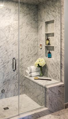 a bathroom with marble walls and flooring has a glass shower door that is open