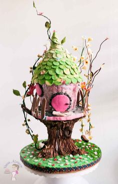 a cake decorated like a tree house on top of a green base with leaves and flowers